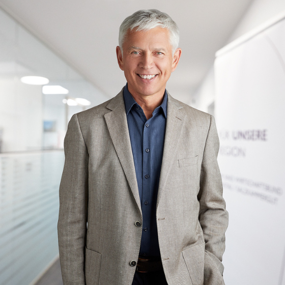 Weißer Mann mit grauen Haaren im Anzug steht in einem Ganz. Er lächelt.