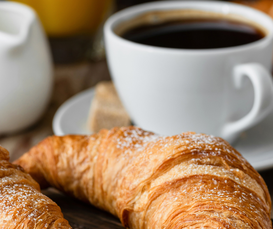 Kaffeetasse mit Cafe im Hintergrund, Croissant im Vordergrund