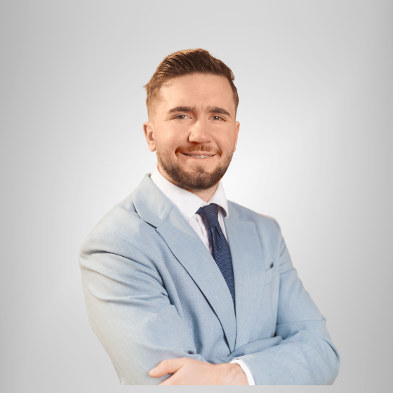 Mann in hellblauem Anzug mit dunkelblauer Krawatte und weißem Hemd. Lächelt in die Kamera, Portraitaufnahme mit verschränkten Händen.