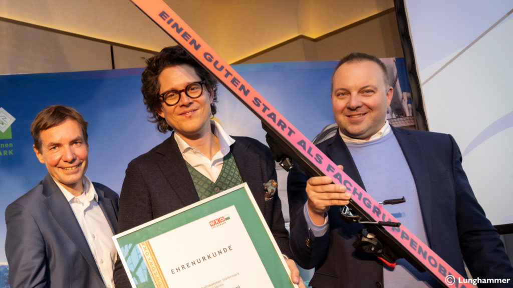 Drei Personen bei einer Staffelübergabe halten eine Ehrenurkunde und ein Paar Skier mit der Aufschrift „Einen guten Start als Fachgruppenobmann