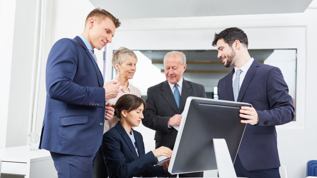 Mehrere Personen in Businesskleidung besprechen gemeinsam Inhalte an einem Computerbildschirm in einem modernen Büro.