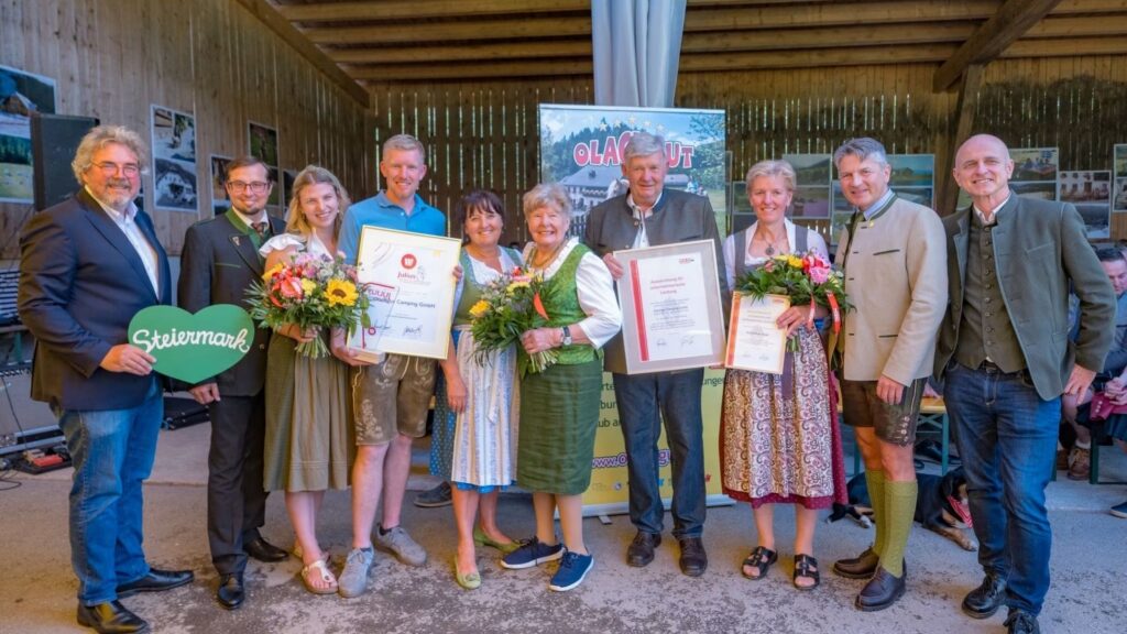 Mehrere Personen stehen bei einer Jubiläumsveranstaltung des Olachguts vor einer Veranstaltungskulisse und präsentieren Urkunden, Blumensträuße sowie die Julius-Award-Auszeichnung. Die Aufnahme entstand im Rahmen des 40-jährigen Bestandsjubiläums des Familienbetriebes in St. Georgen am Kreischberg. Das Bild dokumentiert die Würdigung der erfolgreichen Betriebsentwicklung sowie die Bedeutung des Unternehmens für Tourismus, Beschäftigung und regionale Wertschöpfung.