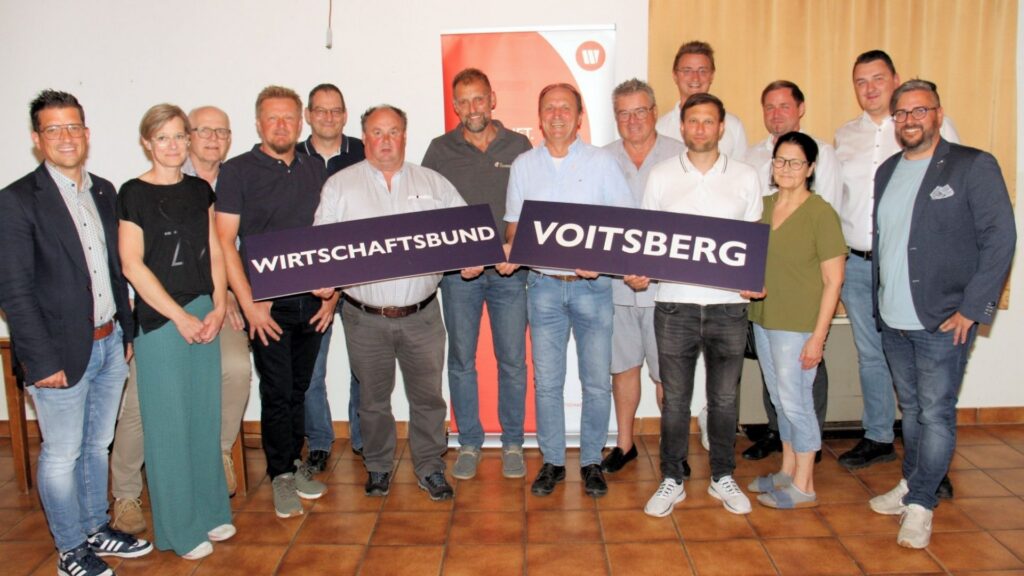 Mitglieder und Funktionäre des Wirtschaftsbundes Krottendorf-Gaisfeld stehen für ein Gruppenfoto vor einem Wirtschaftsbund-Roll-up. In der Mitte halten sie zwei große Schilder mit der Aufschrift „Wirtschaftsbund Voitsberg“.