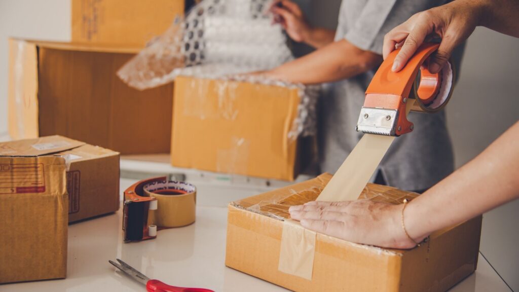 Eine Person verpackt mehrere Kartons mit Klebeband und Luftpolsterfolie für den Versand.